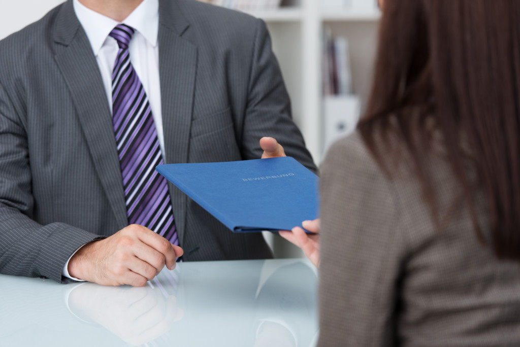 Male business executive giving a female executive a folder of job responsibilities.