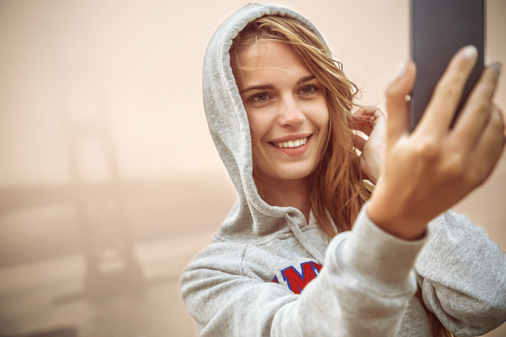 Young woman taking a selfie in front of a bridge.